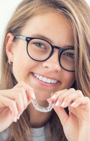 woman with glasses holding up invisalign