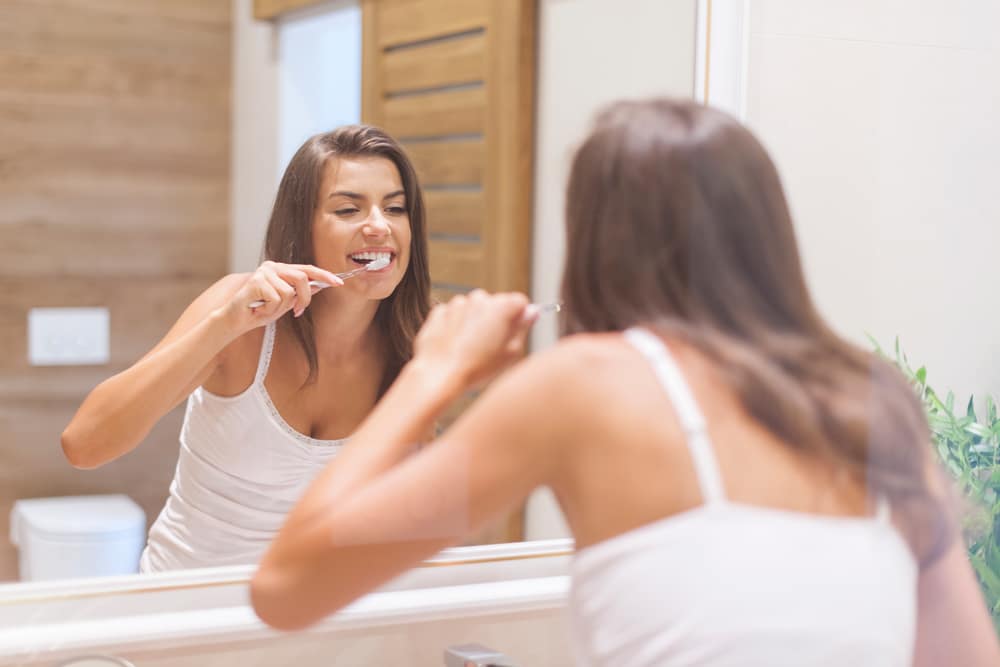 Woman Brushing Teeth In Front Of A Mirror