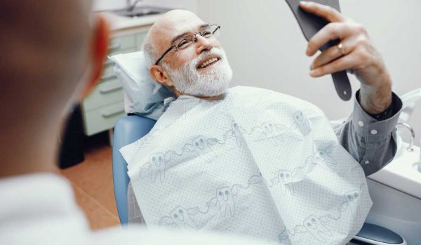 Old Man Looking His Teeth In The Mirror — Dentist In Gosford, NSW