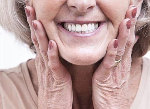 older woman holding mouth smiling with dentures