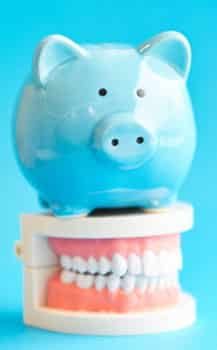 blue piggy bank sitting on top of dentures to resemble affordable dental