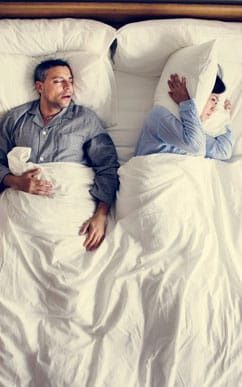 man snoring and wife covering head with pillow