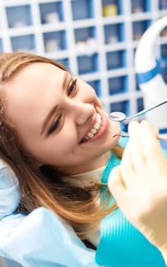 woman smiling as dentist holds up tools